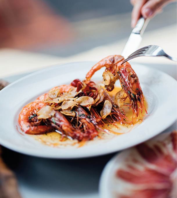 A plate of Spanish-style grilled shrimps, cooked with lemon juice, olive oil and sea salt  With Jamon Iberico in the background  Garlic prawn on a fork 