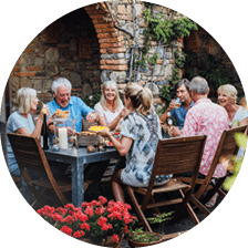 A group of mature friends are sitting around an outdoor dining table, eating and drinking  They are all talking happily and enjoying each others company  The image has been taken in Tuscany, Italy 