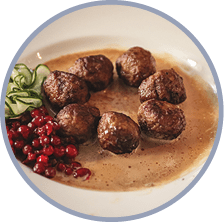 The famous classic Swedish meatballs with red berries, slices of cucumber and brown gravy sauce served in a white plate on dark table top, Stockholm, landmark of Sweden 